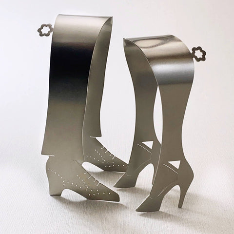 High heel and tap shoe shaped stainless steel serving tongs standing up on grey background