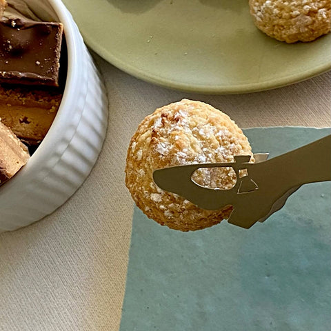 Stainless steel mini tongs holding biscuit next to two plates of biscuits