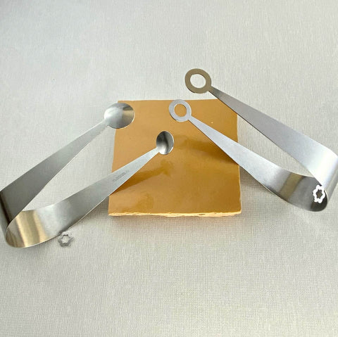 Stainless steel serving tongs in dome and circle design resting on yellow ceramic coaster
