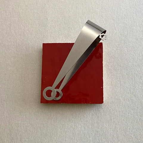 Stainless steel serving tongs with circle design on ends lying on red ceramic coaster