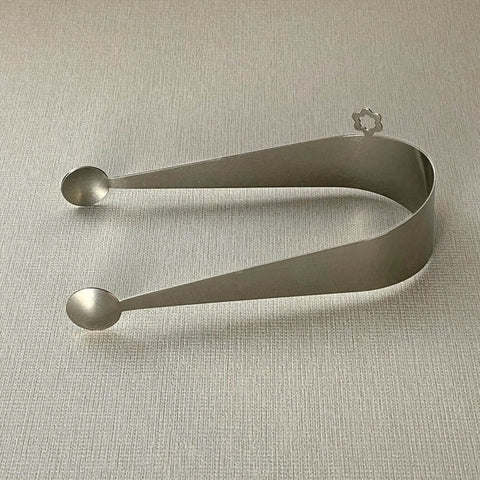 Stainless steel serving tongs with dome ends lying on side on grey background