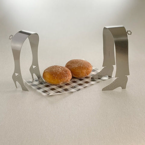 Two pairs of stainless steel shoe shaped serving tongs standing next to two small donuts on checkered paper