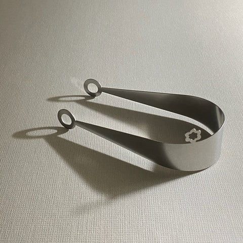 serving tongs stainless steel with circle ends lying on side throwing shadow on light background