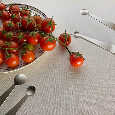 Two stainless steel serving tongs with dome ends next to plate of cherry tomatoes