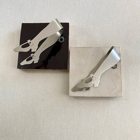 Two stainless steel mini tongs lying on one brown and one white ceramic tiles