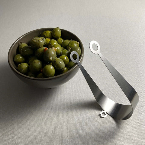 stainless steel serving tongs with circle ends leaning against bowl of gourmet olives