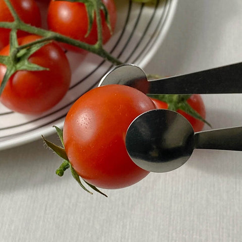 Close up of stainless steel serving tongs with dome end picking up cherry tomato with tomatoes in background