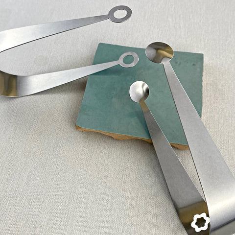 Dome and Circles hand crafted stainless steel serving tongs leaning on blue ceramic coaster