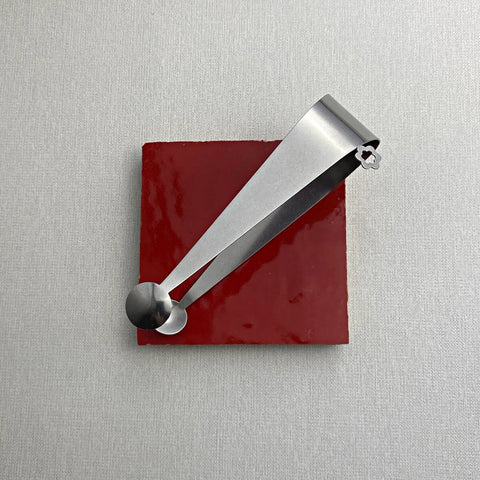 Hand crafted stainless steel serving tongs with dome end resting on red ceramic coaster