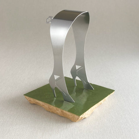 Stainless steel serving tongs in high heel design standing up on green ceramic tile