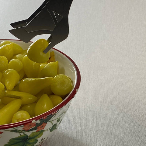 Close up of stainless steel serving tongs in high heel shape picking up small yellow pepper from bowl of peppers
