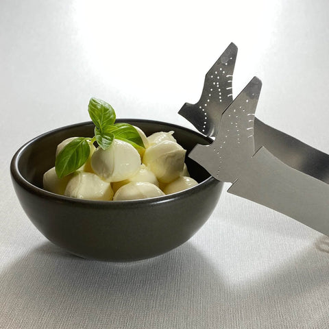 Stainless steel shoe shaped Stepping out tongs leaning against brow bowl with bonconcini balls with basil