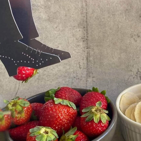 Stainless steel shoe shaped Stepping out serving tongs lifting strawberry from bowl of strawberries
