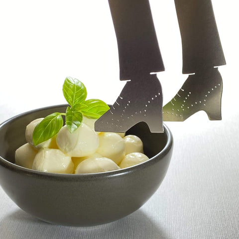 Stainless steel shoe shaped serving tongs hovering over bowl of bonconcini with basil