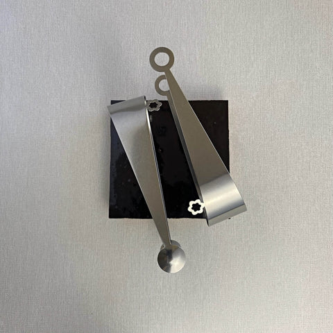 Stainless steel serving tongs in dome and circle design resting on chocolate brown ceramic coaster