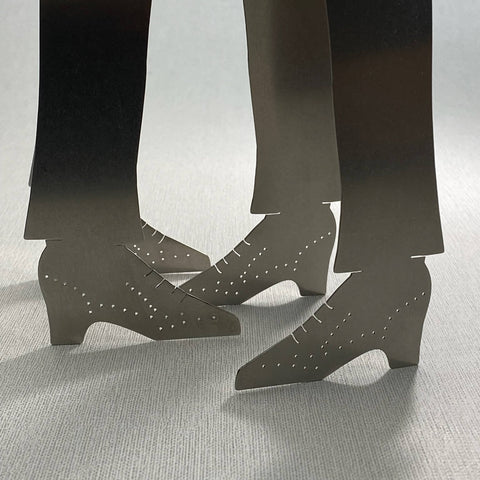 Close up of two shoe shaped stainless steel Stepping Out serving tongs facing eachother on grey background