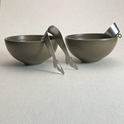 Two brown bowls with two stainless steel mini tongs on light background