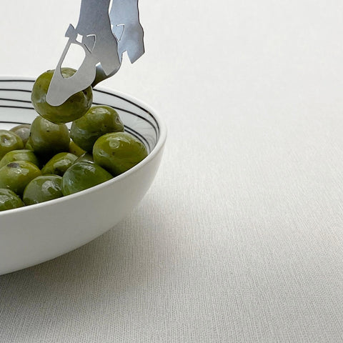 Tip of stainless steel mini tongs picking up olive from white bowl with olives