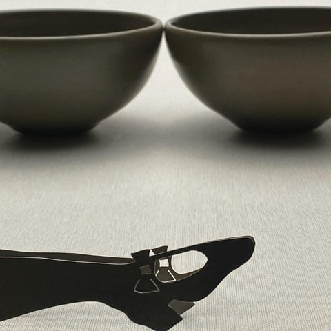 Two brown ceramic bowls with mini stainless steel serving tongs lying in front