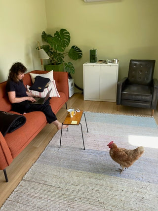 Between You and Me maker working on a laptop in the studio lounge with a chicken nearby