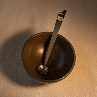 Cabriole stainless steel tiny serving ladle resting in a dark ceramic bowl