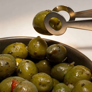 Close-up of Circles stainless steel serving tongs lifting marinated green olive