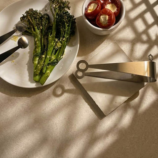 Stainless steel Dome and Circles serving pieces beside grilled broccolini and stuffed mini peppers on Soft Cream table tile on a stone surface 