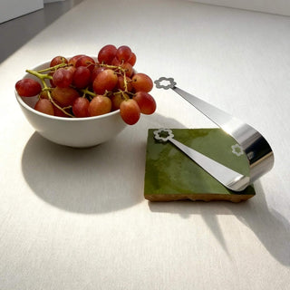Handcrafted stainless steel Flowers serving tongs beside bowl of red grapes on green ceramic tile