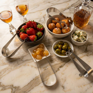Stainless steel Kaleidoscope, Flowers, Dome and Circles serving pieces arranged with strawberries, olives, cheese and arancini on marble