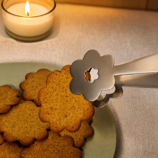Close-up of Kaleidoscope stainless steel server lifting a flower-shaped biscuit beside a lit candle