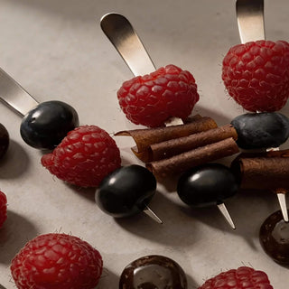 Stainless steel Maestro cocktail picks threaded with raspberries, blueberries and fruit leather on a stone surface