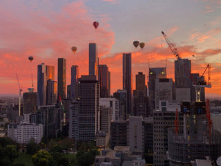 Melbourne city view from Between you and me office studio with tall buildings and hot air balloons against a vibrant sunset sky.