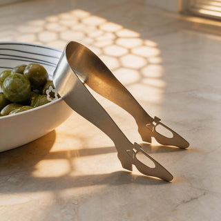 Handcrafted stainless steel Off to see the Wizard serving  piece beside bowl of green olives in warm natural light