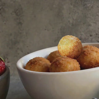 Video of the Kaleidoscope handcrafted stainless steel servers lifting an arancini ball from a white bowl, showing the flower-shaped ends catching the light.