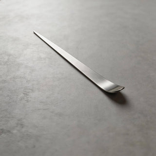 Single handcrafted stainless steel Maestro cocktail pick on a grey stone surface