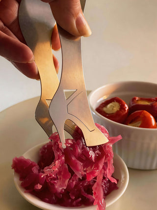 Handcrafted stainless steel high heel serving piece lifting pickled cabbage from small white serving bowl