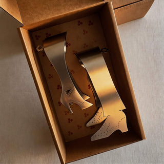 Pair of handcrafted stainless steel Stepping Out serving pieces presented in patterned kraft gift box with warm evening light