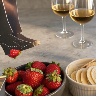 Handcrafted stainless steel tap shoe serving piece lifting strawberry beside bowls of fruit and white wine glasses