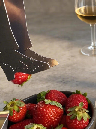 Handcrafted stainless steel tap shoe server lifting strawberry from bowl of strawberries beside white wine glass