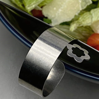 Close-up of Those Two stainless steel salad server handle with flower detail, resting on salad bowl rim